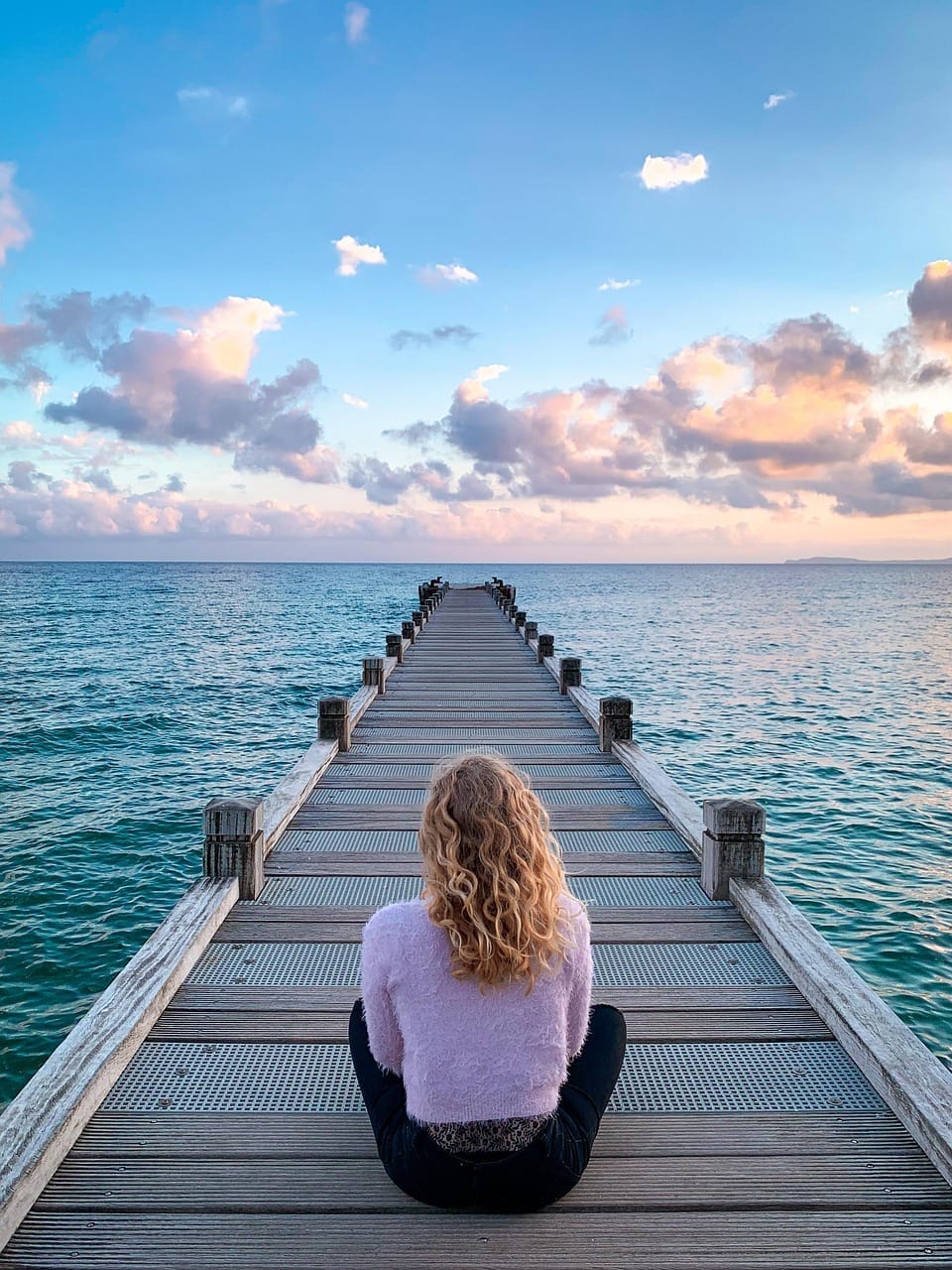 Frau auf Steg ins Meer blickend