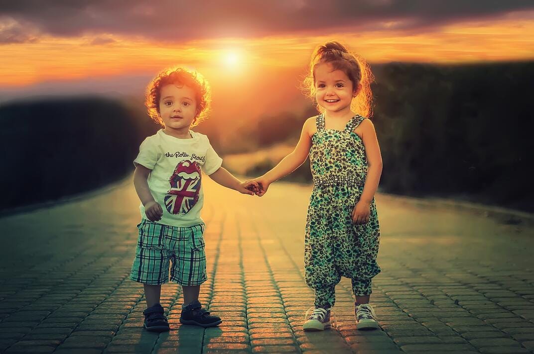 zwei fröhlich schauende Kinder, die sich an der Hand halten. 